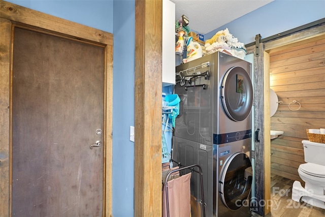 laundry area featuring hardwood / wood-style flooring, a barn door, stacked washer and dryer, and wooden walls