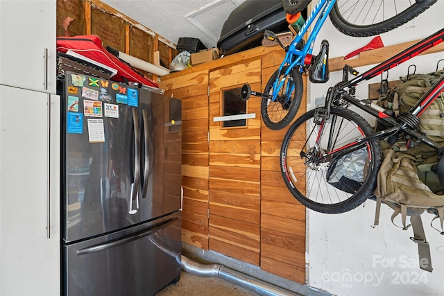 interior space featuring wood walls, stainless steel fridge, a textured ceiling, and concrete floors