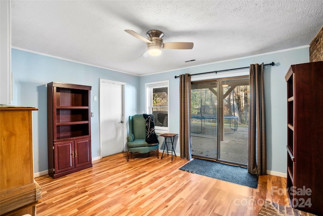 living area featuring a textured ceiling, light wood-type flooring, ceiling fan, and ornamental molding