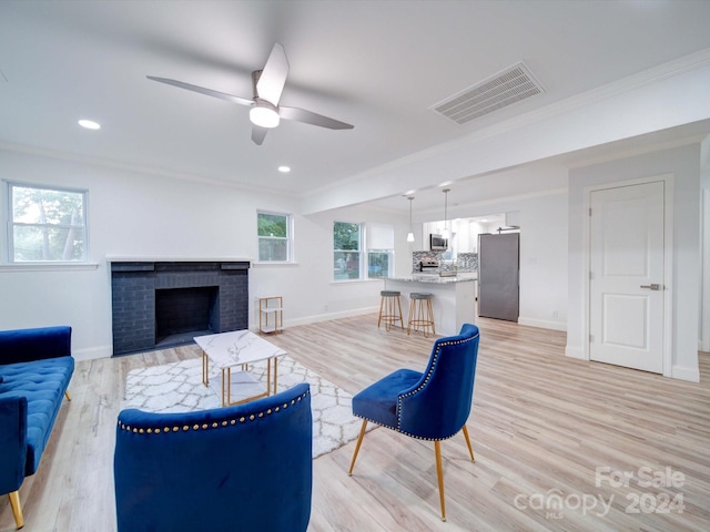 living room featuring ceiling fan, light hardwood / wood-style floors, ornamental molding, and a fireplace