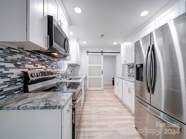 kitchen featuring appliances with stainless steel finishes, light stone counters, a barn door, white cabinets, and light hardwood / wood-style floors