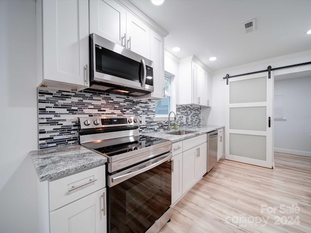 kitchen featuring white cabinets, a barn door, backsplash, and appliances with stainless steel finishes