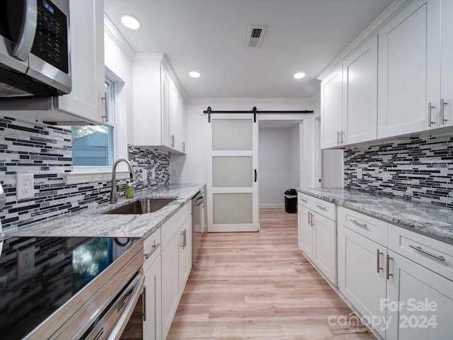 kitchen with white cabinets, a barn door, sink, and stainless steel appliances