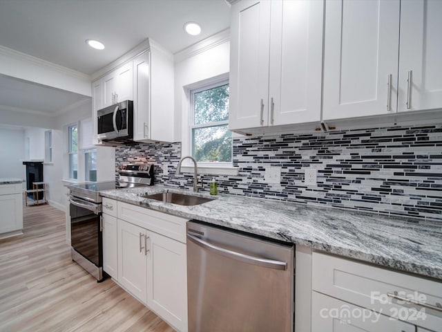 kitchen with white cabinets, crown molding, sink, light wood-type flooring, and appliances with stainless steel finishes