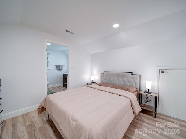 bedroom with ensuite bathroom, lofted ceiling, and light wood-type flooring