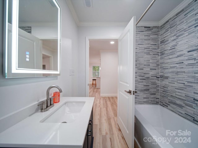 bathroom featuring wood-type flooring, vanity, tiled shower / bath combo, and ornamental molding