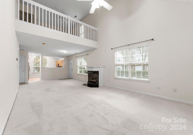 unfurnished living room with light carpet, high vaulted ceiling, plenty of natural light, and ceiling fan