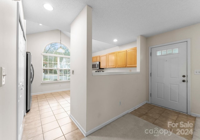 kitchen with light brown cabinetry, appliances with stainless steel finishes, a textured ceiling, lofted ceiling, and light tile patterned flooring