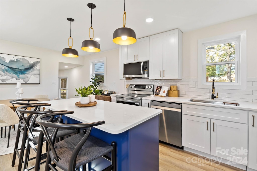 kitchen featuring sink, hanging light fixtures, appliances with stainless steel finishes, white cabinets, and light wood-type flooring