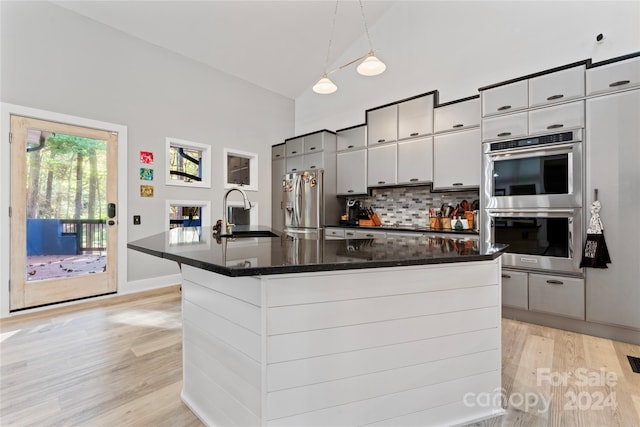 kitchen featuring appliances with stainless steel finishes, decorative light fixtures, a kitchen island with sink, and sink