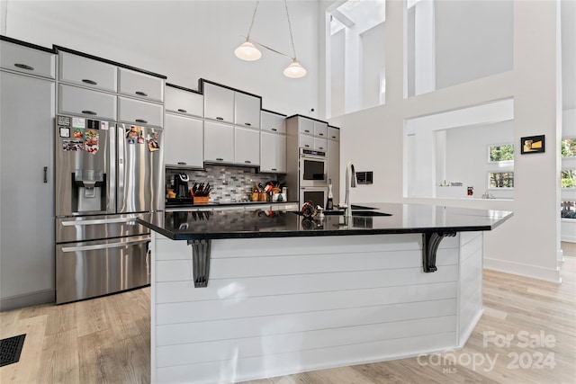 kitchen with sink, light hardwood / wood-style flooring, decorative light fixtures, a kitchen bar, and stainless steel appliances