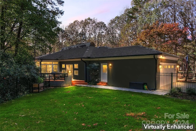 back house at dusk with a garage, cooling unit, and a lawn