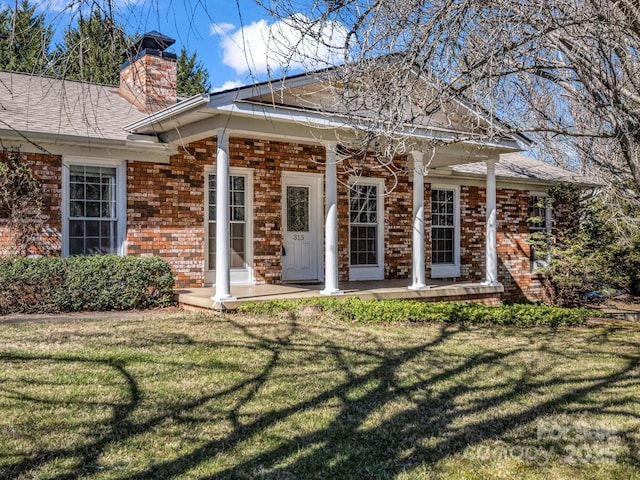 rear view of property featuring a yard, a chimney, covered porch, and brick siding