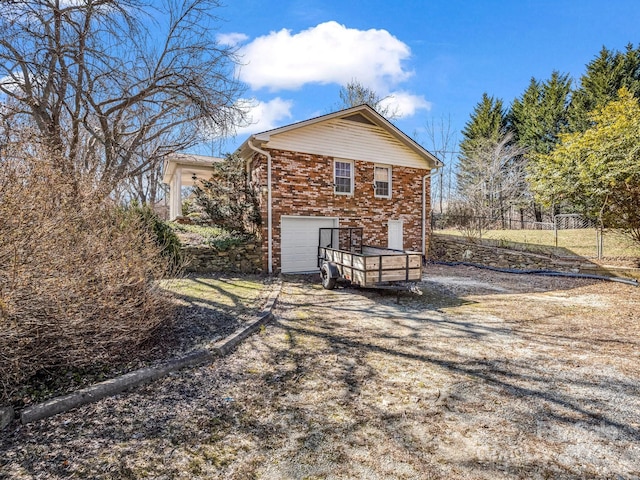 rear view of property with a garage, driveway, fence, and brick siding