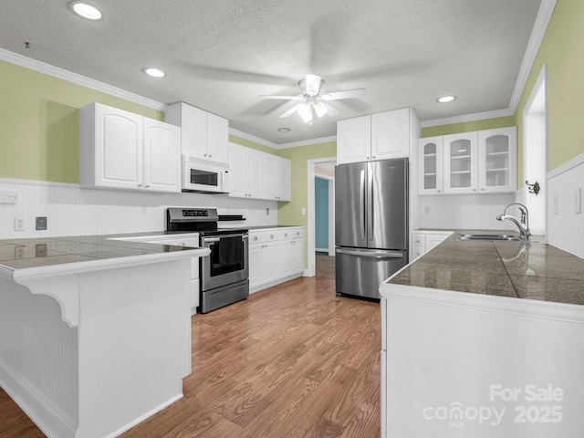 kitchen featuring tile counters, glass insert cabinets, a peninsula, stainless steel appliances, and a sink