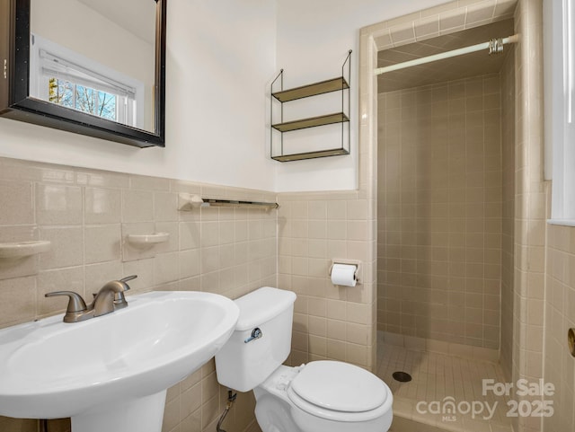 full bathroom featuring toilet, a wainscoted wall, a sink, a shower stall, and tile walls