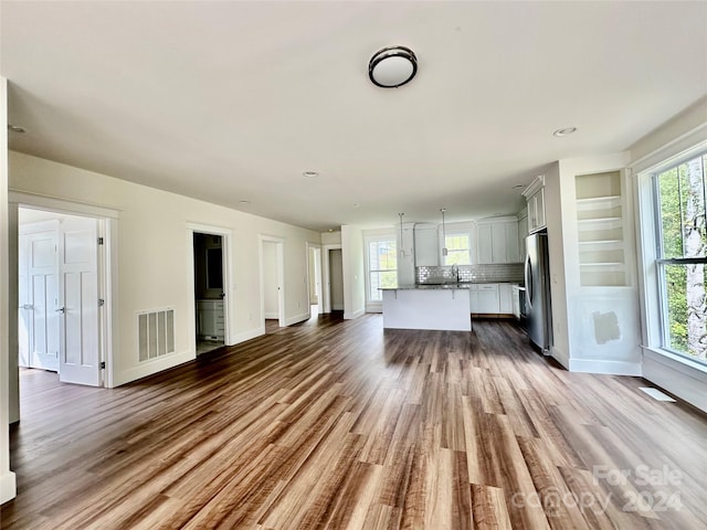 unfurnished living room with light hardwood / wood-style flooring, a healthy amount of sunlight, built in features, and sink