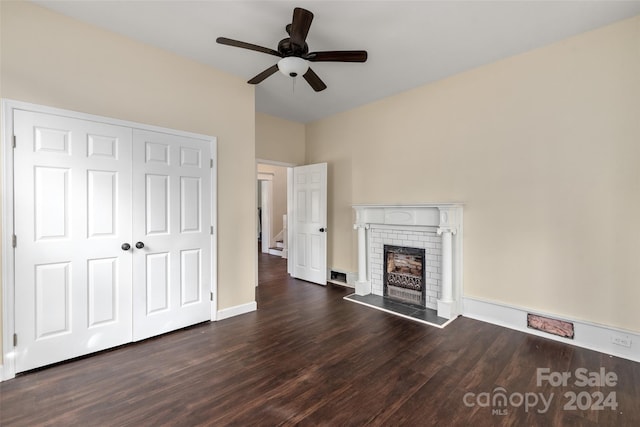 unfurnished living room featuring a brick fireplace, ceiling fan, and dark wood-type flooring