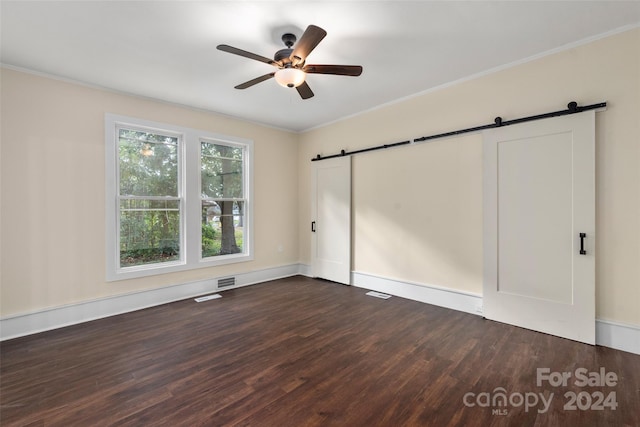 unfurnished bedroom featuring ceiling fan, a barn door, crown molding, and dark wood-type flooring