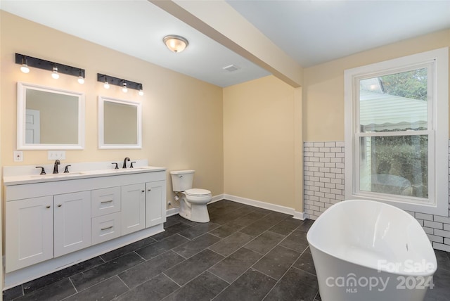 bathroom featuring a washtub, vanity, toilet, and tile walls