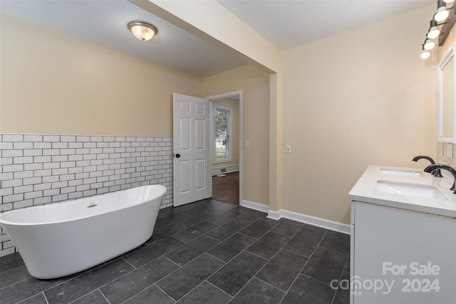 bathroom with a tub to relax in, tile patterned floors, vanity, and tile walls