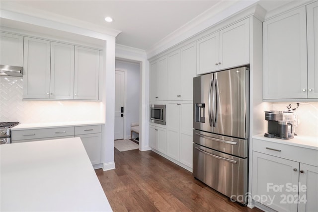 kitchen with appliances with stainless steel finishes, dark hardwood / wood-style flooring, tasteful backsplash, ornamental molding, and extractor fan