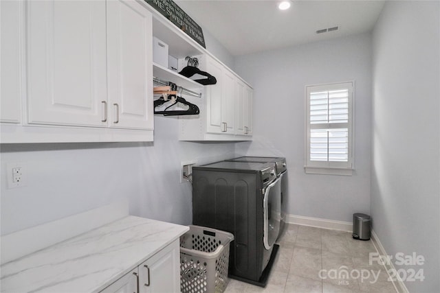 clothes washing area featuring cabinets, light tile patterned flooring, and washer and dryer