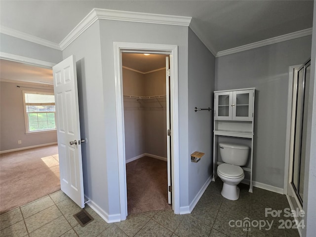 bathroom with tile patterned flooring, toilet, a shower with door, and crown molding