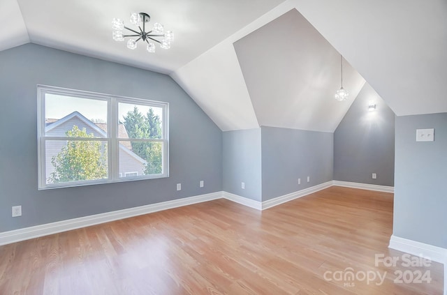 additional living space featuring a notable chandelier, light wood-type flooring, and vaulted ceiling