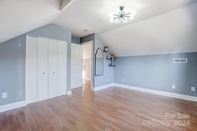 additional living space with an inviting chandelier, light wood-type flooring, and vaulted ceiling