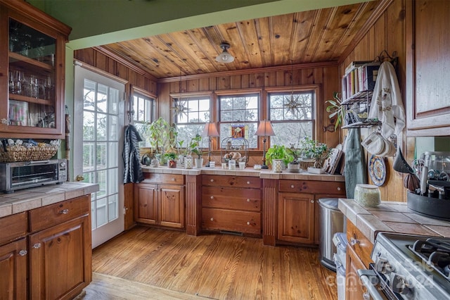 kitchen with wooden walls, tile counters, a healthy amount of sunlight, and light wood-type flooring