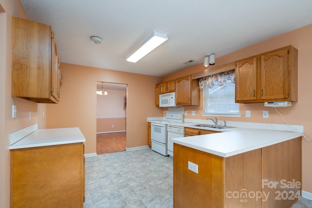 kitchen featuring a textured ceiling, kitchen peninsula, sink, and white appliances