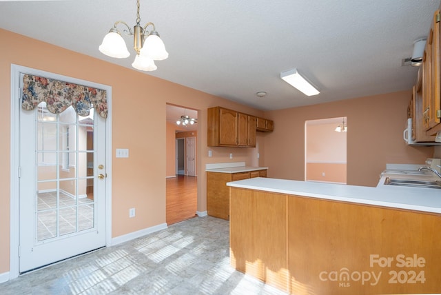 kitchen with stove, sink, decorative light fixtures, a notable chandelier, and kitchen peninsula