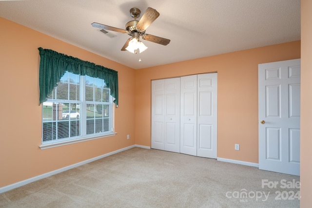 unfurnished bedroom with light carpet, a textured ceiling, a closet, and ceiling fan