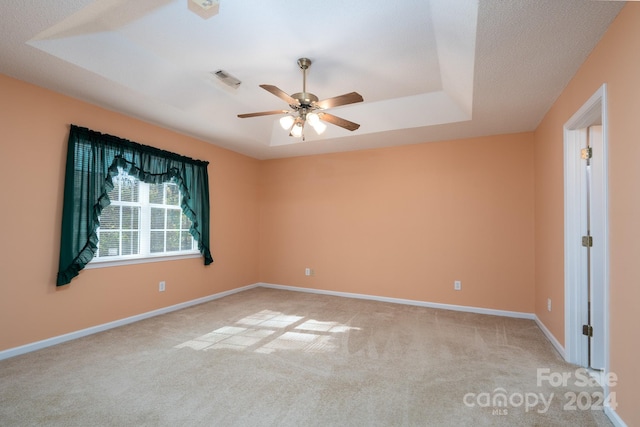 carpeted empty room featuring ceiling fan, a raised ceiling, and a textured ceiling