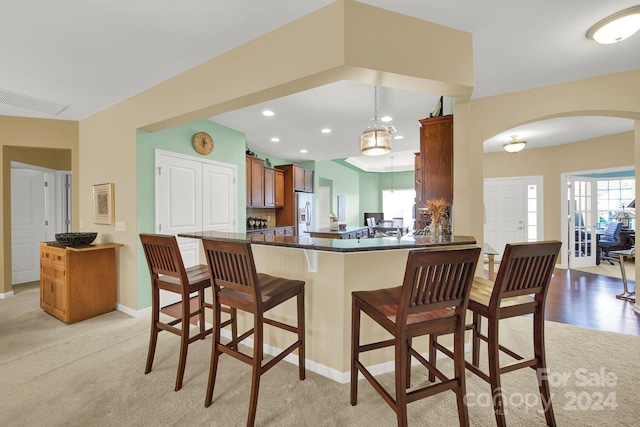 kitchen with light carpet, kitchen peninsula, hanging light fixtures, a kitchen bar, and stainless steel fridge with ice dispenser