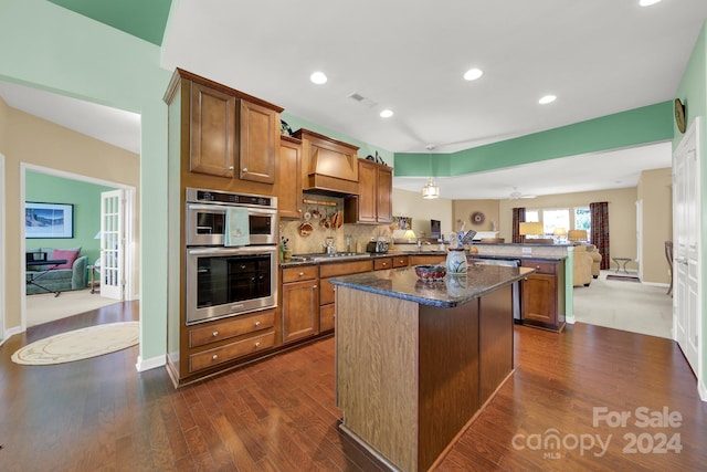 kitchen with kitchen peninsula, stainless steel appliances, a center island, dark hardwood / wood-style floors, and hanging light fixtures