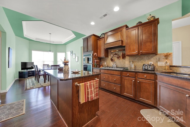 kitchen featuring a center island, dark hardwood / wood-style floors, premium range hood, pendant lighting, and decorative backsplash