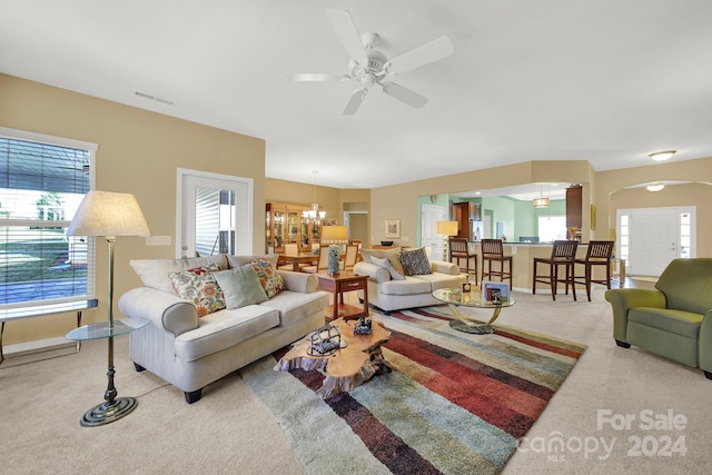 carpeted living room with ceiling fan with notable chandelier