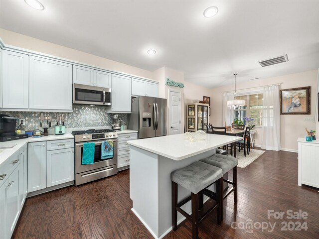 kitchen featuring appliances with stainless steel finishes, dark hardwood / wood-style flooring, a kitchen island, hanging light fixtures, and a breakfast bar area