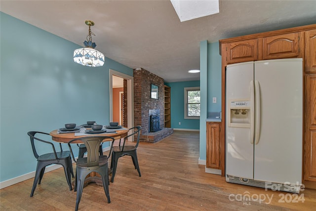 dining area featuring light wood-type flooring, a textured ceiling, and a brick fireplace