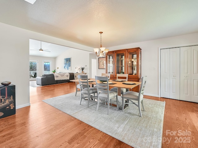 dining room featuring ceiling fan with notable chandelier, light hardwood / wood-style floors, and vaulted ceiling