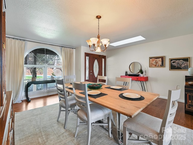 dining space with a skylight, wood-type flooring, a textured ceiling, and an inviting chandelier