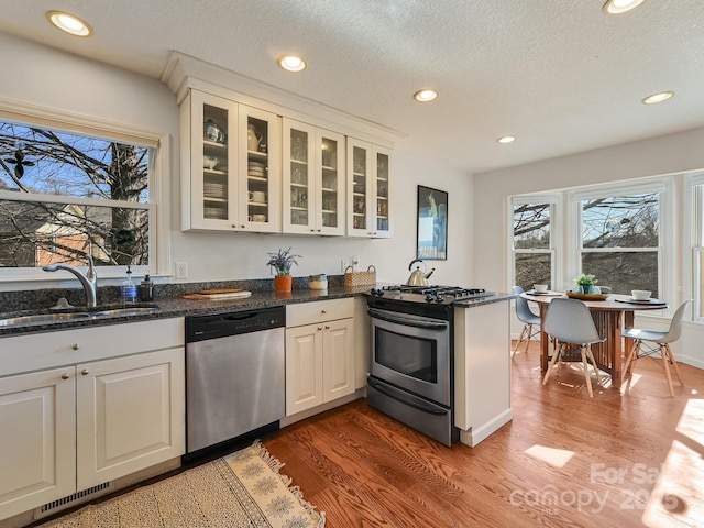 kitchen with appliances with stainless steel finishes, sink, dark stone countertops, white cabinets, and hardwood / wood-style floors