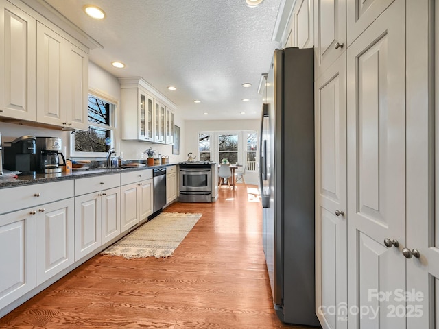 kitchen with dark stone counters, white cabinets, a textured ceiling, light hardwood / wood-style floors, and stainless steel appliances