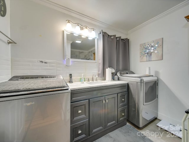 bathroom featuring washer and clothes dryer, vanity, crown molding, and backsplash