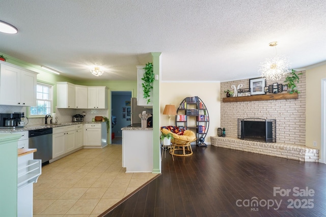 kitchen with sink, dishwasher, white cabinets, a brick fireplace, and light wood-type flooring