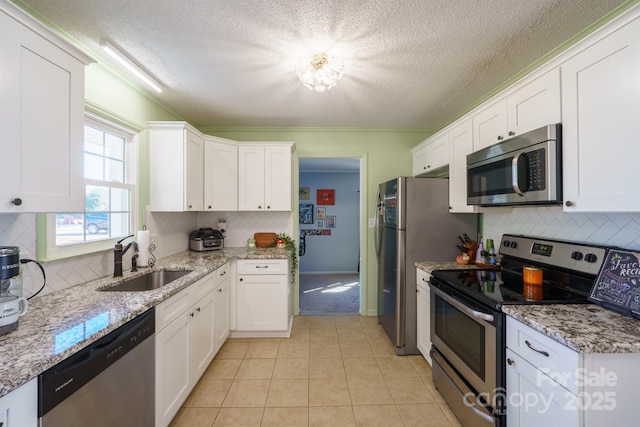 kitchen with light tile patterned flooring, sink, light stone counters, stainless steel appliances, and white cabinets