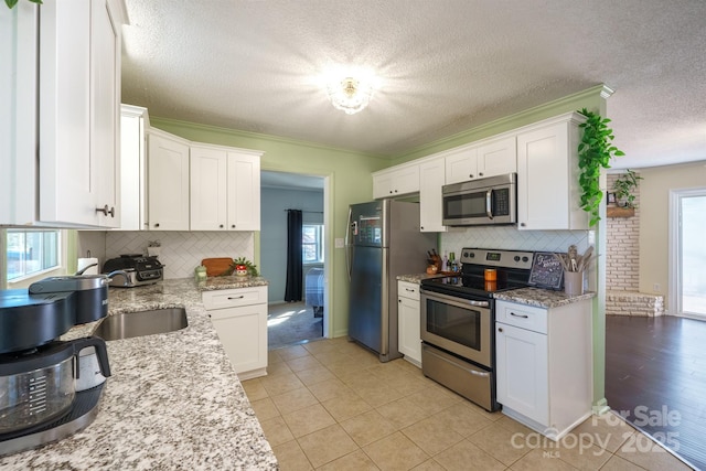 kitchen with stainless steel appliances, white cabinetry, and light stone counters