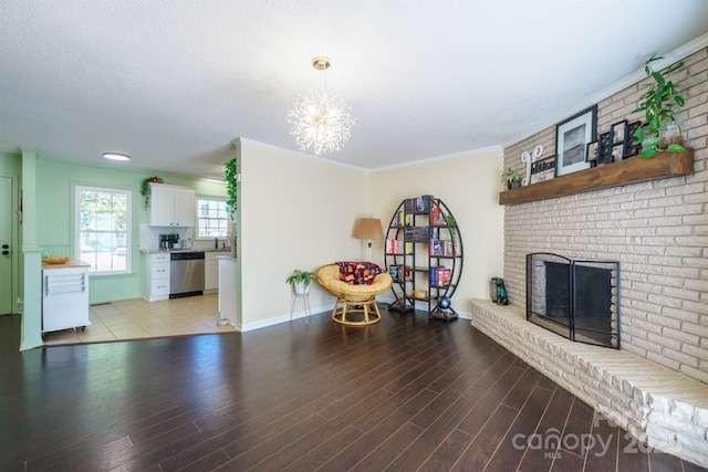 living room with crown molding, a notable chandelier, a brick fireplace, and light wood-type flooring